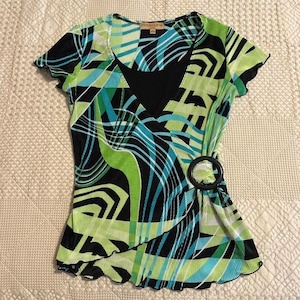 May include: A short-sleeved top with a vibrant abstract pattern in black, green, and teal. The top features a V-neckline, a black circular buckle, and the brand name "notations". The fabric is pleated.