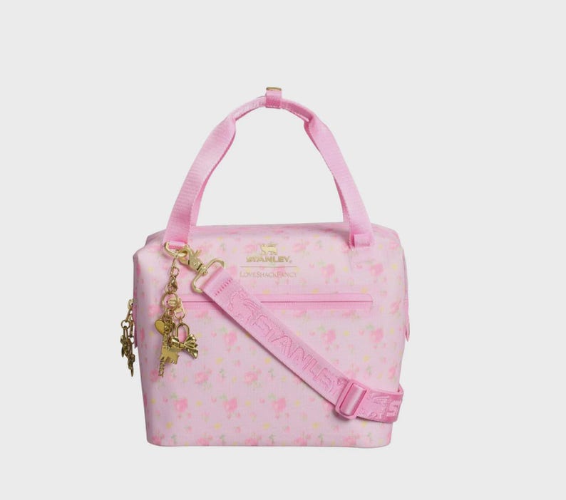 Pode incluir: Bolsa tote rosa isolada com padr&atilde;o floral, al&ccedil;a de ombro remov&iacute;vel e al&ccedil;a superior. A bolsa tem pingentes dourados e a inscri&ccedil;&atilde;o "STANLEY" na al&ccedil;a. Ideal para transportar objetos.