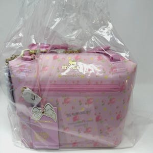 Pode incluir: Bolsa rosa com padr&atilde;o floral, al&ccedil;a de corrente dourada e z&iacute;per. A bolsa tem uma etiqueta com um la&ccedil;o branco e texto. A bolsa &eacute; embrulhada em pl&aacute;stico transparente. A bolsa tem o texto "STANLEY".