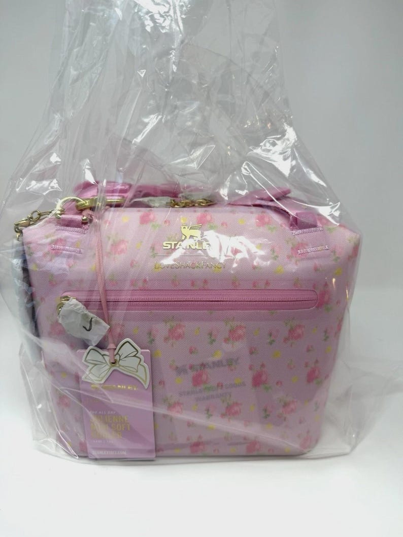 Pode incluir: Bolsa rosa com padr&atilde;o floral, al&ccedil;a de corrente dourada e z&iacute;per. A bolsa tem uma etiqueta com um la&ccedil;o branco e texto. A bolsa &eacute; embrulhada em pl&aacute;stico transparente. A bolsa tem o texto "STANLEY".