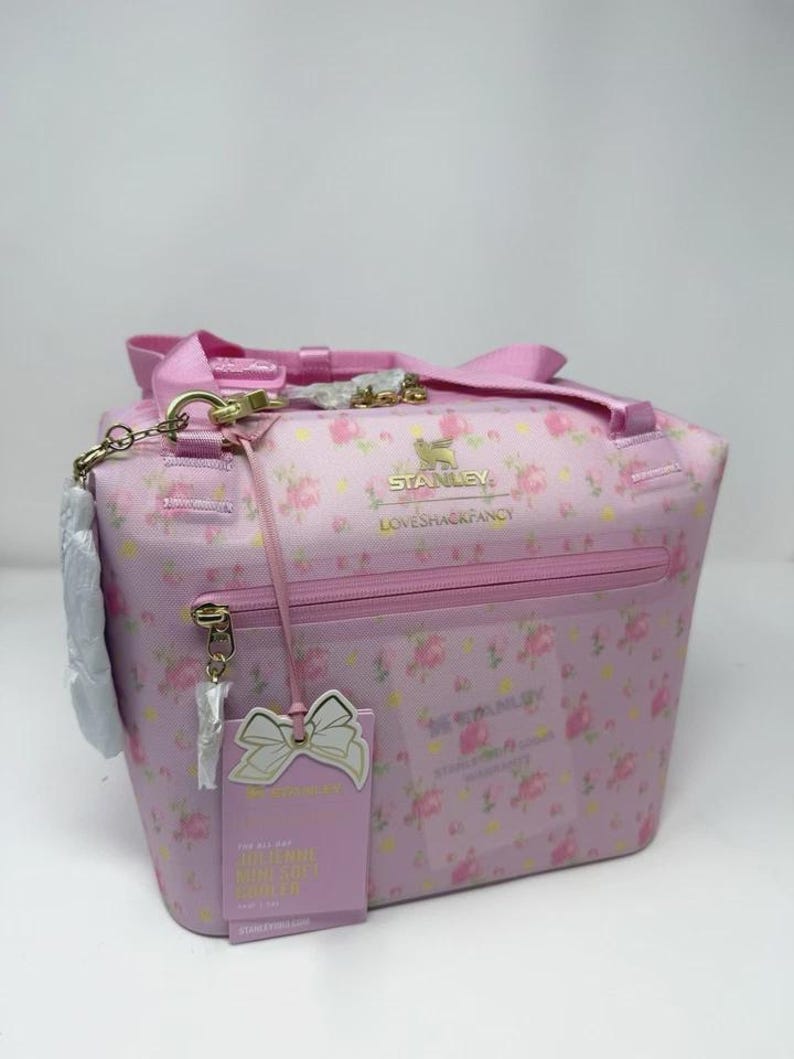 Pode incluir: Bolsa t&eacute;rmica rosa com estampa floral, al&ccedil;a superior e la&ccedil;o decorativo. A bolsa tem fecho de z&iacute;per e uma etiqueta com o texto "FOR ALL DAY MILLENNIAL COOLER". A bolsa tem o texto "STANLEY LOVESHACKFANCY".
