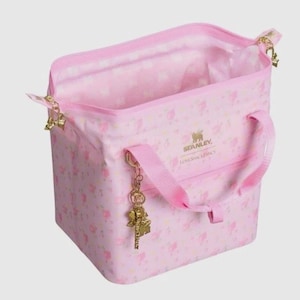 Pode incluir: Uma bolsa tote rosa com um padr&atilde;o floral e o texto "STANLEY LOVESHACKFANCY". A bolsa tem uma al&ccedil;a superior, uma al&ccedil;a de ombro e um pingente dourado. A bolsa est&aacute; aberta, revelando um interior rosa.