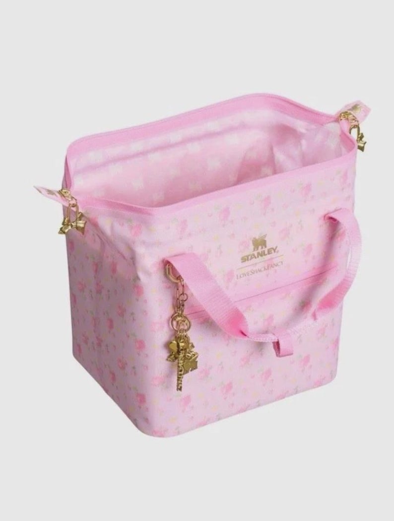 Pode incluir: Uma bolsa tote rosa com um padr&atilde;o floral e o texto "STANLEY LOVESHACKFANCY". A bolsa tem uma al&ccedil;a superior, uma al&ccedil;a de ombro e um pingente dourado. A bolsa est&aacute; aberta, revelando um interior rosa.