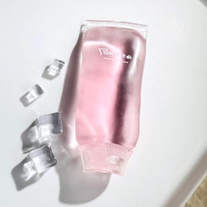 May include: A translucent pink squeeze tube with a ribbed cap and base, featuring the white text "Pawoto" and "handmade with love" printed on the front. Four clear, square ice cubes are positioned to the left of the tube on a white surface.