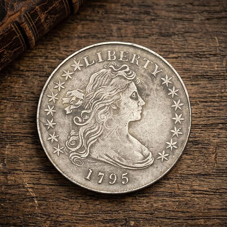 May include: A silver coin with the word "LIBERTY" arched across the top. The coin features a profile of a woman's face, surrounded by stars and the date "1795". The coin is set against a dark wooden surface.