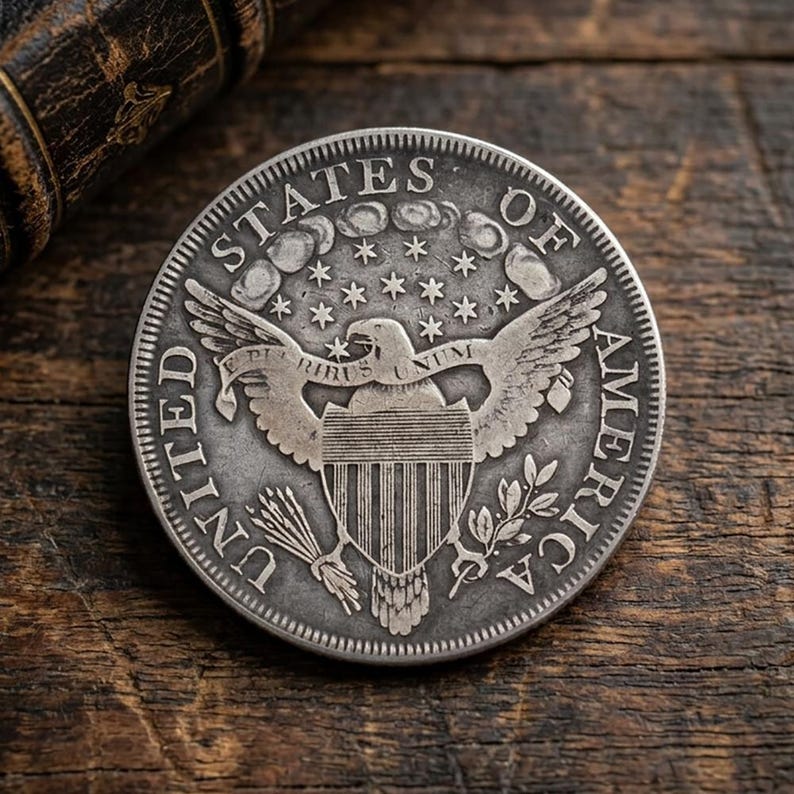 Może przedstawiać: Szczeg&oacute;łowa srebrna moneta z orłem z rozpostartymi skrzydłami, gwiazdami i napisem "UNITED STATES OF AMERICA". Moneta spoczywa na rustykalnej drewnianej powierzchni, podkreślając jej postarzany wygląd i wartość historyczną.