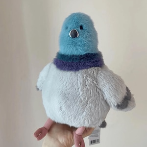 K&ouml;nnte beinhalten: Ein Pl&uuml;schpigeon mit blauem Kopf, lila-blauem Kragen und grauem K&ouml;rper. Das Spielzeug hat kleine schwarze Augen, einen kleinen Schnabel und rosa F&uuml;&szlig;e. Der Pigeon ist weich und flauschig und scheint ein Stofftier zu sein.