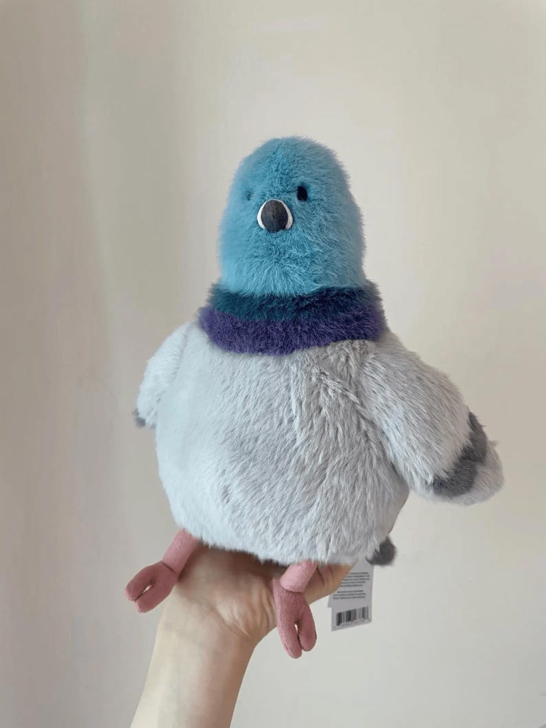 K&ouml;nnte beinhalten: Ein Pl&uuml;schpigeon mit blauem Kopf, lila-blauem Kragen und grauem K&ouml;rper. Das Spielzeug hat kleine schwarze Augen, einen kleinen Schnabel und rosa F&uuml;&szlig;e. Der Pigeon ist weich und flauschig und scheint ein Stofftier zu sein.