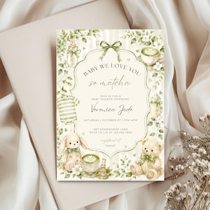 Puede incluir: Invitación a un baby shower con diseño de acuarela. La invitación presenta el texto "Baby We Love You So Matcha" e incluye ilustraciones de un osito de peluche, un conejito y ropa de bebé. La invitación está sobre un fondo crema.