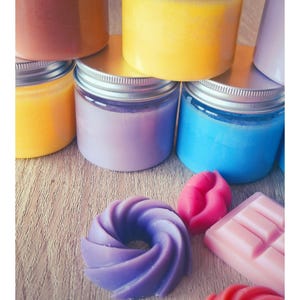 Peut inclure: Une collection de pots en plastique transparent avec des couvercles à vis argentés remplis de cire colorée, notamment jaune, bleue, violette et orange. À côté des pots se trouvent des cires parfumées en forme de spirales, de lèvres et de tablette.