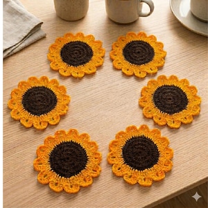 Könnte beinhalten: Sechs handgefertigte Häkeluntersetzer im Sonnenblumen-Design. Jeder Untersetzer hat eine dunkelbraune Mitte und gelbe Blütenblätter, angeordnet auf einer hellen Holzoberfläche. Die Untersetzer sind rund und haben ein strukturiertes Aussehen.