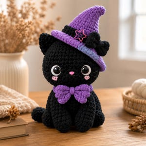 May include: A handmade black crochet cat wearing a purple witch hat with a pink star and a purple bow tie. The cat has large white eyes, pink cheeks, and a pink nose. The cat is sitting on a wooden surface.