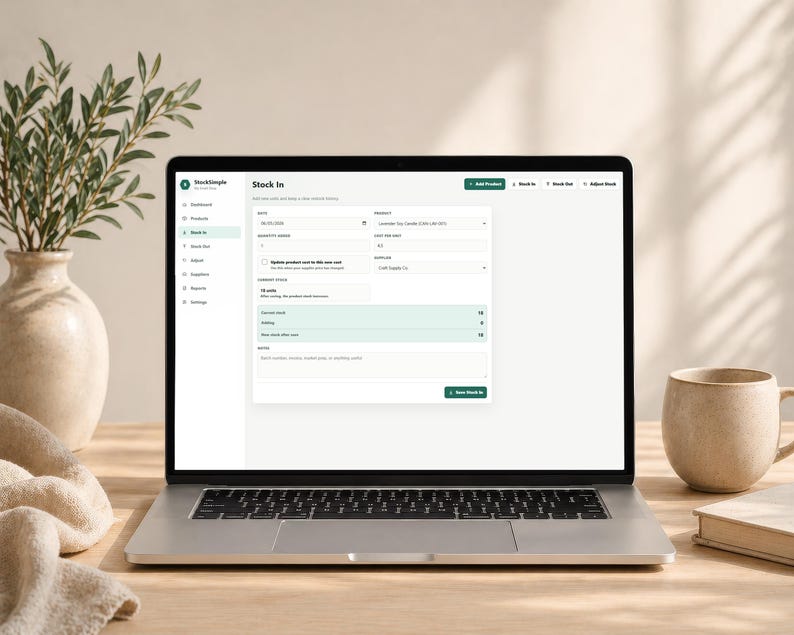 Pode incluir: Um laptop exibindo uma interface "Stock In" com detalhes do produto. A tela mostra campos para quantidade, data e outras informa&ccedil;&otilde;es de invent&aacute;rio. Uma caneca bege, um livro e um vaso decorativo com vegeta&ccedil;&atilde;o est&atilde;o na mesa de madeira.