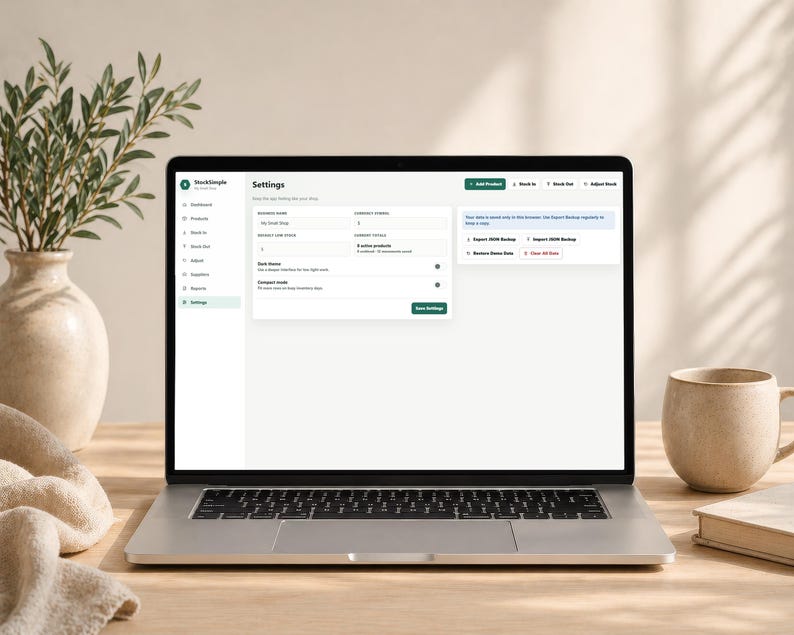 Pode incluir: Um laptop exibindo a p&aacute;gina "Configura&ccedil;&otilde;es" de um aplicativo de software. A tela mostra v&aacute;rias op&ccedil;&otilde;es de configura&ccedil;&otilde;es, incluindo contagens de produtos e recursos de exporta&ccedil;&atilde;o de dados. Uma caneca bege, um livro e um vaso decorativo com vegeta&ccedil;&atilde;o est&atilde;o na mesa de madeira.