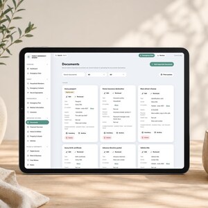 May include: A tablet displaying a digital family emergency binder interface with a sidebar menu and a main dashboard showing organized document cards for passports, insurance, licenses, birth certificates, and directives with edit and review options.