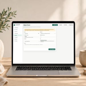 Pode incluir: Um laptop exibindo a interface "Ajustar Estoque" do aplicativo StockSimple. A tela mostra detalhes do invent&aacute;rio. Uma caneca bege e um livro est&atilde;o &agrave; direita. Um vaso com vegeta&ccedil;&atilde;o e um pano dobrado est&atilde;o &agrave; esquerda.