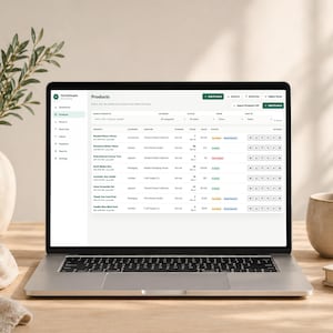 Pode incluir: Um laptop exibindo um painel de controle de gerenciamento de estoque de produtos. A tela mostra detalhes do produto, categorias e n&iacute;veis de estoque. Uma caneca bege, um livro e um vaso com vegeta&ccedil;&atilde;o est&atilde;o na mesa de madeira.
