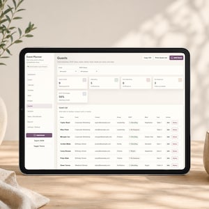 May include: A black tablet displays an event planner interface with guest details. The screen shows a list of guests, their RSVP status, and other event-related information. A vase with a plant and a ceramic cup are in the background.