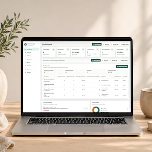 Pode incluir: Um laptop exibindo uma interface de painel com dados de invent&aacute;rio. A tela mostra detalhes do produto, n&iacute;veis de estoque e m&eacute;tricas financeiras. Um vaso com vegeta&ccedil;&atilde;o, uma caneca e um livro est&atilde;o na mesa de madeira.