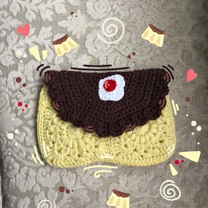 May include: A handmade crochet pouch featuring a pale yellow rectangular base and a dark brown scalloped flap. The flap is adorned with a central white circular patch topped with a small red sphere, resembling a dessert with a cherry on top.