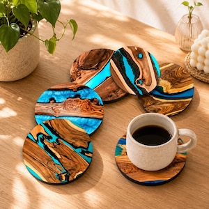 May include: A set of five circular coasters made from natural wood slices and bright turquoise resin. Each coaster features unique wood grain patterns and a smooth finish. One coaster supports a speckled white ceramic mug filled with coffee.