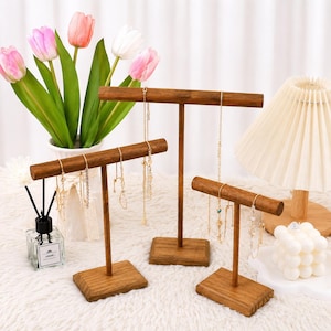 May include: Three T-shaped wooden jewelry display stands of varying heights, each featuring a horizontal bar supported by a central post and a rectangular base. The stands are crafted from dark brown wood and are used to hang delicate gold necklaces.