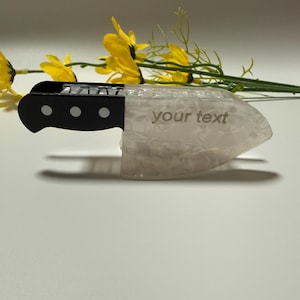 Könnte beinhalten: Ein dekoratives Messerobjekt mit schwarzem Griff und klarer, strukturierter Klinge. Der Text "your text" ist auf der Klinge eingraviert. Gelbe Blumen sind im Hintergrund.