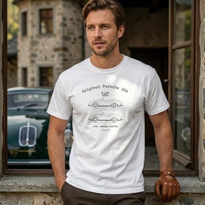 Può includere: T-shirt bianco con grafica nera di una Porsche 356. Il testo "Original Porsche 356" è sopra le illustrazioni dell'auto. Sotto, il testo "1948 - GMUND, AUSTRIA Porsche". La persona indossa guanti da guida in pelle marrone.