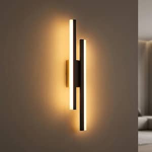 May include: A wall-mounted light fitting featuring two vertical black rectangular bars of unequal length. Each bar contains a central strip of warm white LED light that illuminates the wall behind it, creating a soft glow effect.