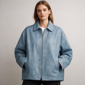 May include: A pale blue jacket with a collar and a full zip. The jacket has two front pockets and is made of a soft, textured material. The model is wearing a white top underneath.
