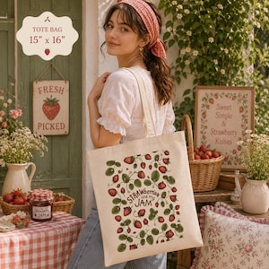 以下が含まれることがあります： イチゴのデザインと「Strawberries are my Jam」の文字が入ったクリーム色のトートバッグ。バッグのサイズは38cm x 41cmです。画像には「Fresh Picked」と書かれた看板とイチゴジャムの瓶も写っています。
