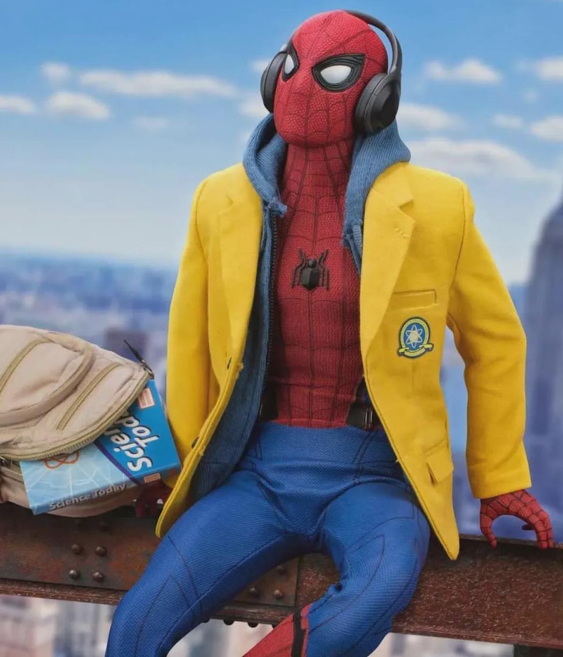 Puede incluir: Figura de acci&oacute;n de Spider-Man con un traje rojo y azul, una sudadera con capucha azul, una blazer amarilla y pantalones azules. La figura lleva auriculares negros y est&aacute; sentada en una viga de metal. Una mochila y un libro est&aacute;n cerca.