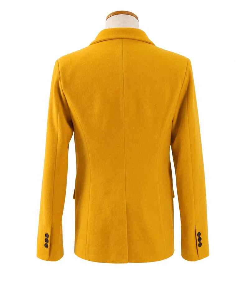 Puede incluir: Un blazer amarillo mostaza con un dise&ntilde;o cl&aacute;sico. La vista trasera muestra un ajuste entallado, solapas con muescas y tres botones en cada manga. El blazer se exhibe en un maniqu&iacute; con cuello de madera.