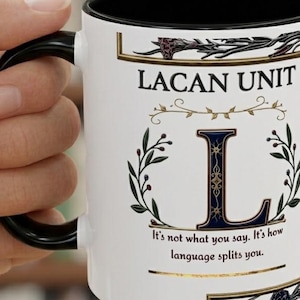 May include: White ceramic mug with a black handle and interior, featuring the text "LACAN UNIT" and a large letter "L". The mug also includes the quote "It's not what you say. It's how language splits you."