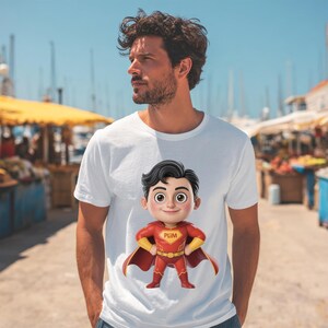 May include: A white short-sleeved t-shirt featuring a centered graphic of a cartoon superhero character with black hair, wearing a red suit with yellow accents, a red cape, and the text PLIM printed on the chest emblem in a yellow font.