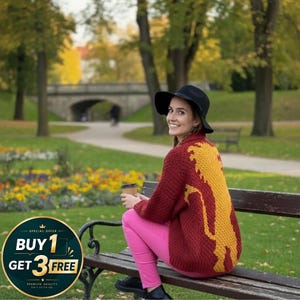 May include: A woman wearing a burgundy sweater with a yellow design, pink pants, and a black hat sits on a park bench. She holds a coffee cup. The background shows a park with trees, flowers, and a bridge.