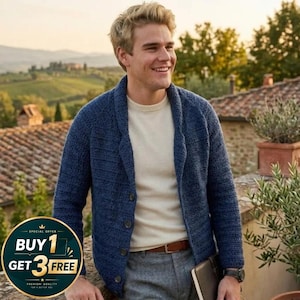 Op de afbeelding: Een blauw gebreid vest met een sjaalkraag en knoopsluiting. Het vest wordt gedragen over een crèmekleurig shirt en gecombineerd met een grijze broek. Een bruine leren riem en een horloge zijn ook zichtbaar.