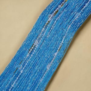 May include: A bright blue string curtain featuring a dense arrangement of vertical threads with a shimmering metallic finish. Interspersed throughout the strands are clear, spherical beads of varying sizes that add texture and light reflection.