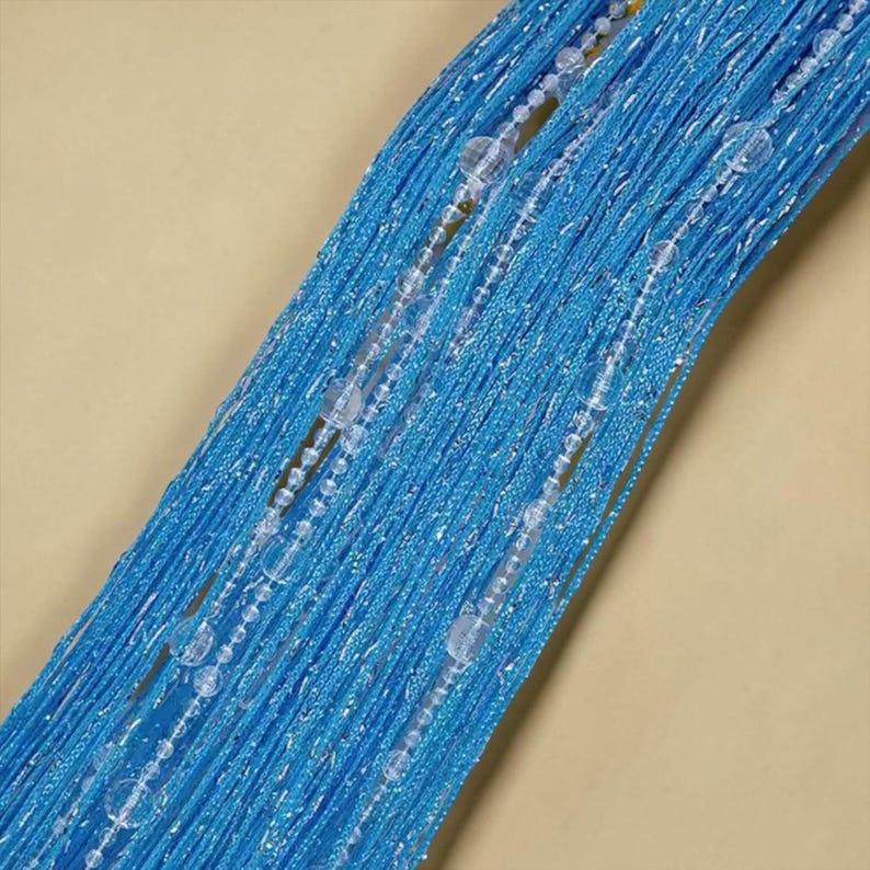 May include: A bright blue string curtain featuring a dense arrangement of vertical threads with a shimmering metallic finish. Interspersed throughout the strands are clear, spherical beads of varying sizes that add texture and light reflection.