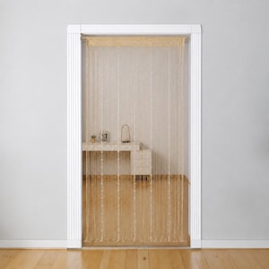 May include: A gold string curtain featuring vertical strands of thin, shimmering metallic threads. The curtain is mounted within a white door frame, hanging straight down to create a semi-transparent partition that allows light to pass through.