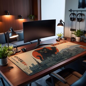 May include: A rectangular desk mat featuring a graphic illustration of a giant black cat looming over a city skyline with a large red sun, Mount Fuji, and Japanese text. The mat is positioned on a dark wood desk surface with a computer monitor.