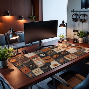 May include: A rectangular desk mat featuring a patchwork pattern of Halloween-themed illustrations including orange pumpkins, white ghosts, black cats, skulls, bats, moths, and autumn flowers in shades of orange, black, white, and grey.