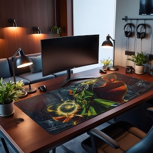May include: A rectangular desk mat featuring a graphic illustration of a hooded figure in a green tunic and red cape casting a glowing yellow energy spell. The mat is positioned on a dark wood desk surface in front of a curved computer monitor.