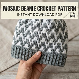 May include: A gray and white mosaic crochet beanie held in a hand. The beanie has a ribbed gray brim and a geometric pattern in white and gray. Text at the top reads "MOSAIC BEANIE CROCHET PATTERN" and "INSTANT DOWNLOAD PDF".