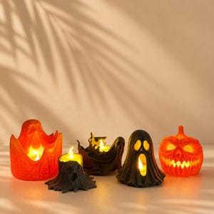 Peut inclure: Un ensemble de cinq bougeoirs sur le thème d'Halloween comprenant une citrouille orange vif, un fantôme noir, une souche d'arbre noire avec un visage, un bol en forme de fantôme noir et un grand bougeoir orange en forme de flamme, tous éclairés.
