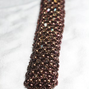 May include: A brown beaded bracelet with a metallic clasp. The beads are a mix of round and faceted, creating a textured look.