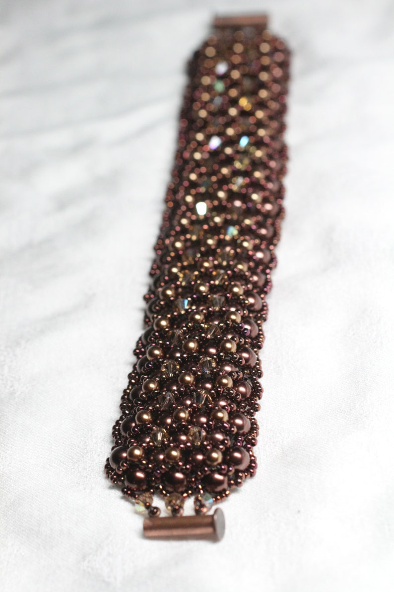 May include: A brown beaded bracelet with a metallic clasp. The beads are a mix of round and faceted, creating a textured look.