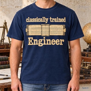 May include: A navy blue short-sleeve t-shirt featuring a graphic print of a vintage slide rule positioned between the text "classically trained" above and "Engineer" below in a distressed, light-coloured, serif font style.