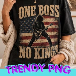 Può includere: T-shirt nero con un design a bandiera americana invecchiata e la silhouette di un chitarrista. Il testo recita "ONE BOSS NO KINGS". Le parole "TRENDY PNG" sono in basso. Il design ha un aspetto vintage.