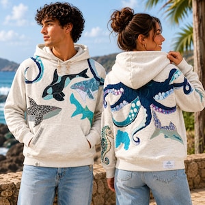 Puede incluir: Dos sudaderas con capucha gris jaspeado claro con aplicaciones de vida marina. La sudadera frontal muestra una orca y un tiburón, mientras que la trasera presenta un pulpo azul oscuro, un caballito de mar y un tiburón con detalles de tela texturizada.
